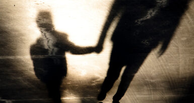Blurry vintage shadow silhouettes of father and son walking hand in hand in old asphalt road  in sepia black and white